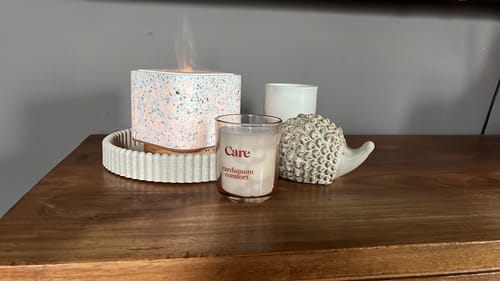 Recensent toont een sfeervol hoekje met een Geurwolkje-verstuiver, kaars en decoratie op een houten meubel.