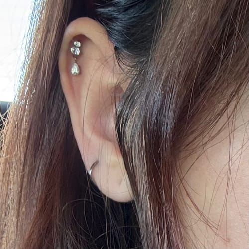 A reviewer's ear showing the Dangle flatback stud silver with a crystal charm in a cartilage piercing.