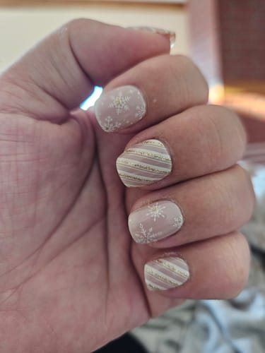 Hand einer Kundin, die die 'Blush Wonderland' UV-Gelfolien trägt und ein Mix-and-Match-Design aus Schneeflocken und Streifen zeigt.