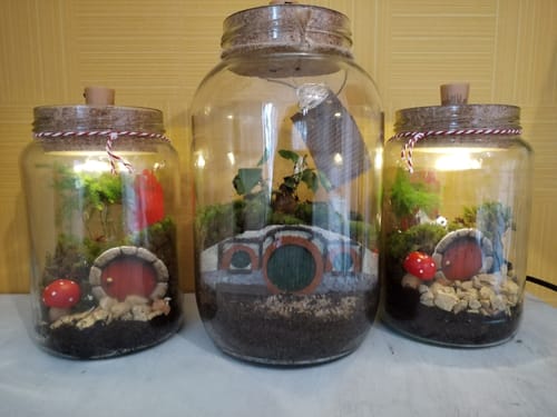 Rezensent zeigt drei gestaltete Halbling-Höhle Flaschengärten: einen großen in der Mitte und zwei kleinere, beleuchtete an den Seiten.