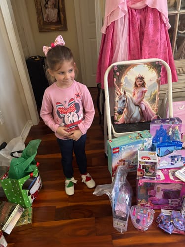 Reviewer's child stands next to their Rose Blossom Unicorn Princess portrait, displayed on a small white easel among gifts.