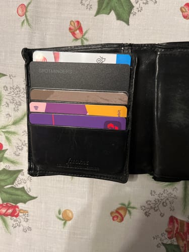 Customer's SPOTMINDERS Tracking Card shown inside a card slot of a black wallet, demonstrating its fit.