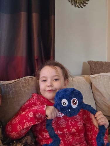 Customer's daughter smiling while holding a fuzzy blue plush monster toy on a couch.