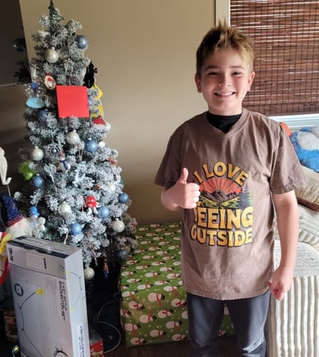 Customer's photo of a person wearing the brown 'I Love Peeing Outside' T-shirt, giving a thumbs-up by a Christmas tree.
