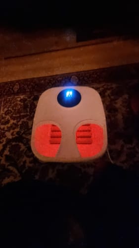 Anmelders tændte Bubble Spa fodmassageapparat i et mørkt rum, med blåt lys på panelet og rødt lys i fodrummene.