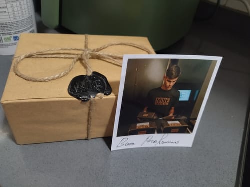 Recensore mostra la confezione del profumo PATCHOULI, legata con spago e sigillo in ceralacca, con accanto una foto.