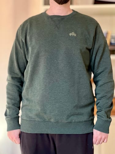 Kunde trägt das grüne, melierte Holzbrüder Unisex Sweatshirt 'Cedar'.