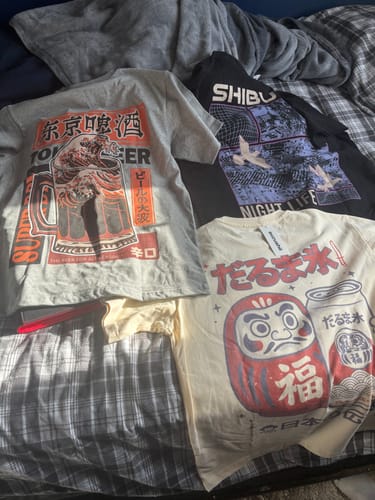 Customer's grey Beer Wave T-Shirt laid out on a bed with two other graphic tees.