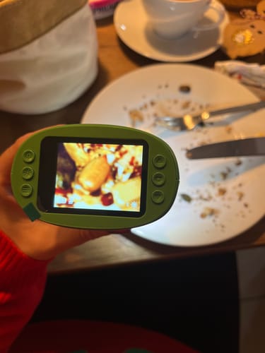 Ein Kunde hält das grüne Edubini Abenteuer-Mikroskop in der Hand, dessen Display vergrößerte Essensreste auf einem Teller zeigt.
