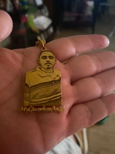Customer holding a gold photo engraved pendant. It shows a man's face and the words 'My Guardian Angel!' on the front.