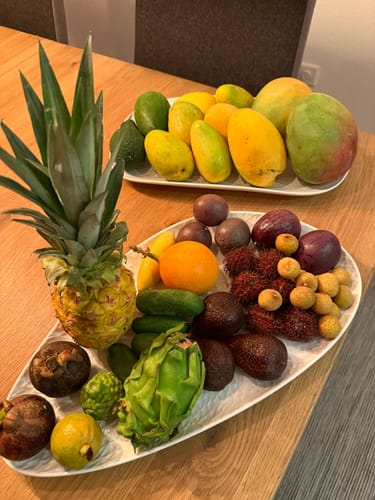 Ein Kunde zeigt die Mangos der Entdeckerbox und weitere exotische Früchte auf zwei weißen Servierplatten.