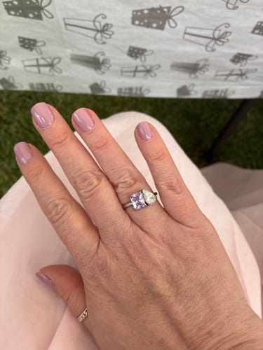 Customer's hand wearing the Toi Et Moi Birthstone Ring with a purple square-cut stone and a clear pear-cut stone.