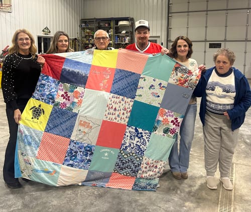 Customers proudly holding their large, colorful Premium T Shirt Quilt made from various shirts.