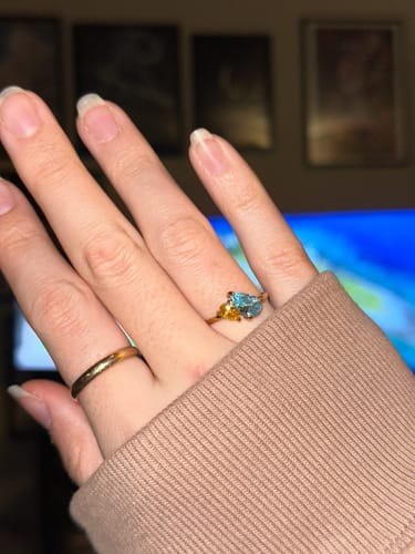 Customer's hand wearing the Leesha Birthstone Ring, showing two pear-cut stones in light blue and yellow on a gold band.