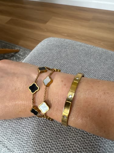Customer's wrist wearing two stacked Celine Clover Bracelets, one with black enamel and one with white mother of pearl.