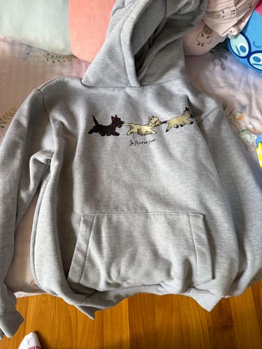 Customer's puppies grey hoodie laid flat on a bed, showing the front graphic of three dogs and the kangaroo pocket.