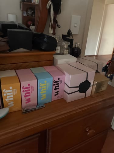 Customer's pink Petal Rush perfume box lined up with other fragrances on a wooden dresser.