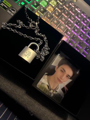 Reviewer's Stray Kids necklace by Hyunjin with its padlock pendant and a photocard, displayed in the open product box.