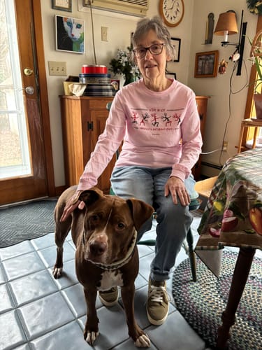Reviewer wearing the pink Stay Wild Petroglyphs Long Sleeve Tee while sitting indoors and petting a dog.