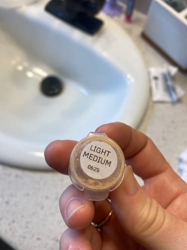 Customer holding a small sample pot of Foundation in the shade 'Light Medium'.