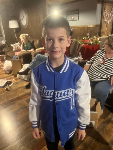 A customer's grandson wearing the custom blue and white varsity jacket with 'Jaguars' and '11' on the front in a living room.
