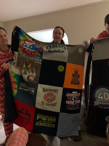 Customers holding a large Premium T Shirt Quilt made from various colorful t-shirts with different logos.