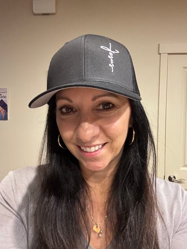 Reviewer wearing the dark gray Jesus Cross hat, showing its fit and white script design on the front panel.