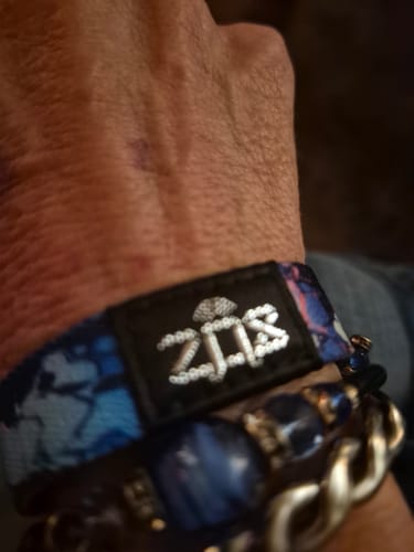 Close-up of a customer's wrist wearing the blue patterned You Are Resilient Interactive Bracelet with other bracelets.