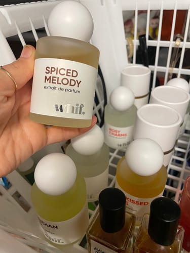 Customer holding a bottle of Spiced Melody perfume, showing its frosted glass and white ball lid in front of a collection.