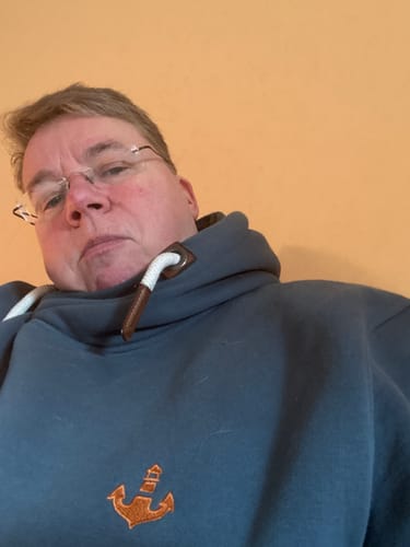 Kundin in einem blaugrauen Pullover mit hohem Kragen und einer orangefarbenen Anker-Stickerei.