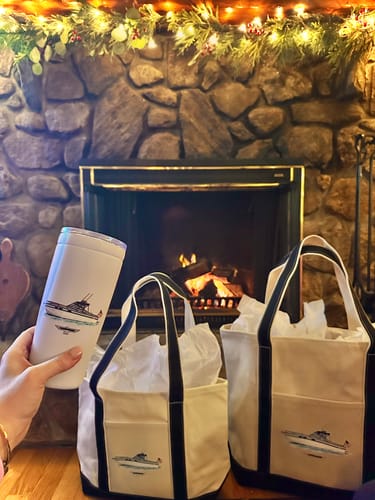 Customer holding a white Custom 20 oz. Boat Tumbler with a boat graphic in front of a fireplace with matching tote bags.