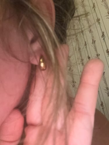 Close-up of a reviewer wearing a single gold Mini Drop Huggie earring.