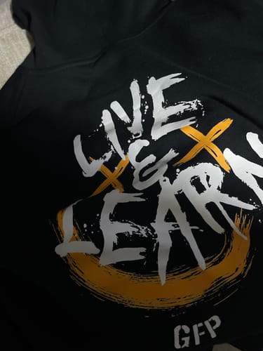 Close-up of a customer's black LIVE & LEARN HOODIE, focusing on the white and orange graphic.