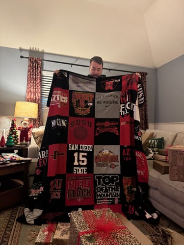 Customer shows a person holding a large Premium T Shirt Quilt made from red and black shirts.