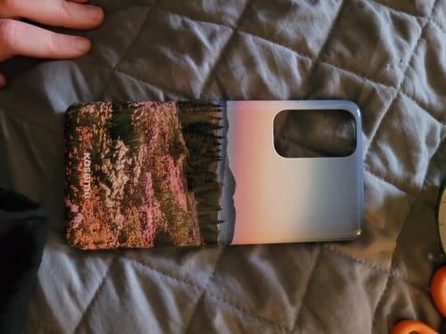 Customer's Sereneproduct phone case with a landscape design and pastel gradient, lying on a grey quilted surface.