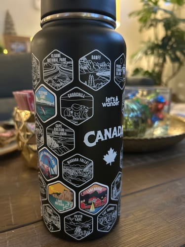Customer's black Canada Bottle with several colorful destination stickers placed over the engraved white outlines.