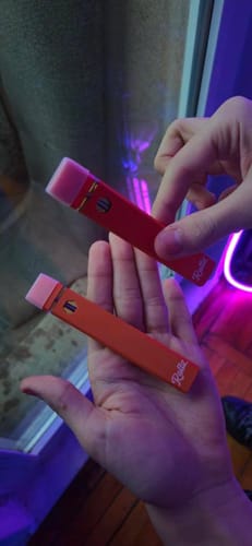 Customer holding two ROLLZ THCA vape pens, one red and one orange, in their hands.