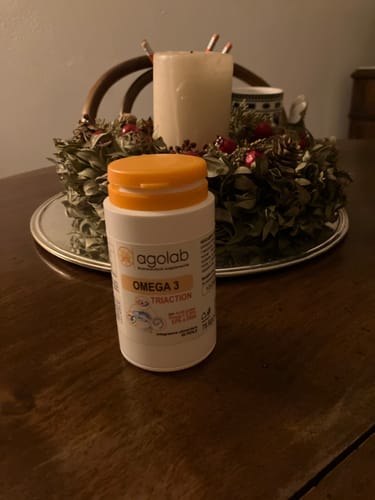 Il recensore mostra il flacone di Omega 3 Tri-Action su un tavolo di legno.