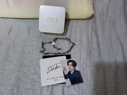 Reviewer's Connect Necklace by Jake displayed with its silver box and a photocard on a bedspread.