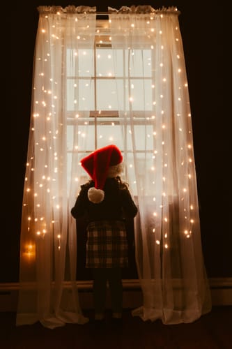Reviewer's photo showing a child in a Santa hat at a window, enhanced with the glowing String Light Overlay Pack.