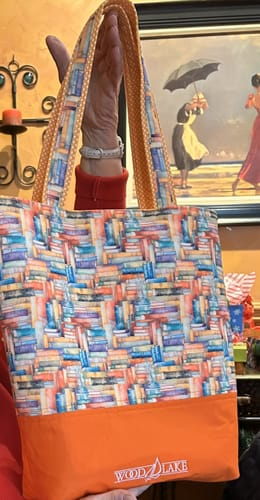Reviewer holding a tote bag made from the Whimsical Colorful Stacked Books Fabric with a solid orange base.