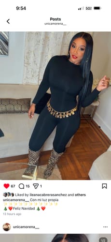 Reviewer posing indoors in the black NW Sculpt Jumpsuit, styled with a gold belt and animal print boots.