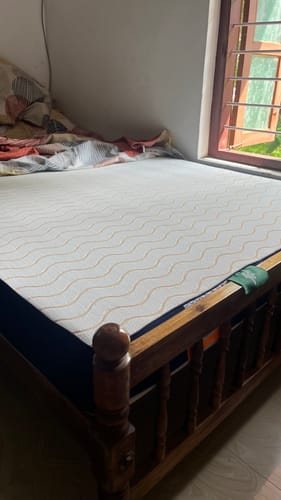 Customer's Flo Mattress Ergo on a wooden bed frame, showing the white cover with a gold wavy pattern.