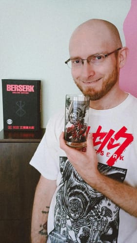 Un cliente sonriente sostiene un vaso Guts transparente, mostrando el diseño detallado de un personaje de Berserk.
