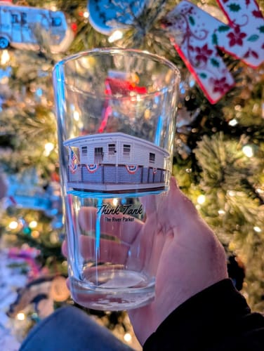 Customer holding a custom pint glass with a printed image of a 'Think Tank' houseboat in front of a Christmas tree.