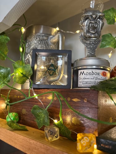 Customer's custom green D20 dice in its display case, on a shelf with fantasy decor and lights.
