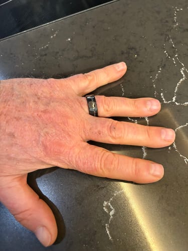 Customer's hand wearing the hammered black Forged Meteorite ring while resting on a dark countertop.