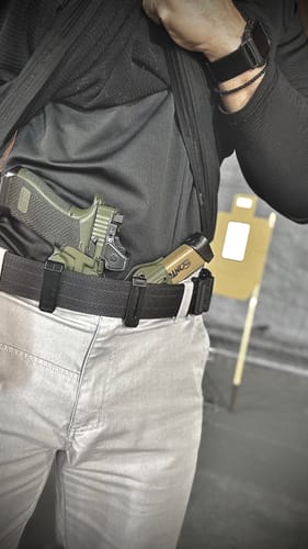Customer shows the olive green APX holster tucked inside their waistband at a shooting range.