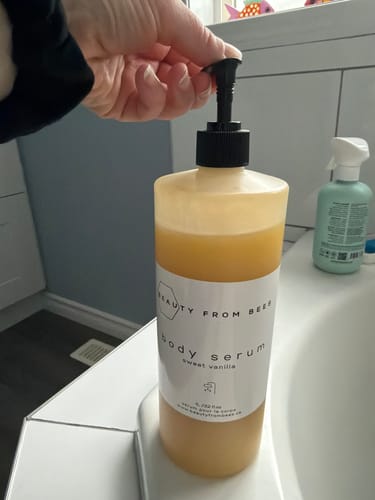 Customer pressing the pump on a bottle of Sweet Vanilla Body Serum in their bathroom.
