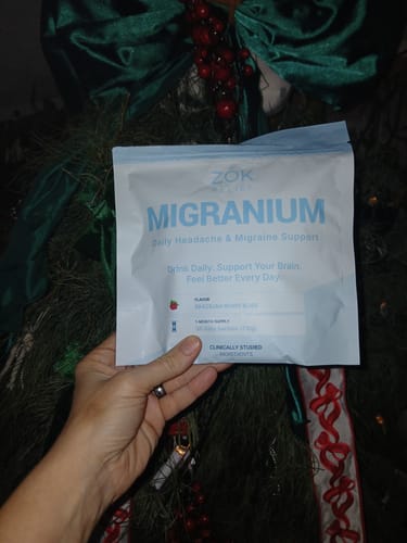 Customer holding the light blue Migranium supplement pouch in front of a green wreath.